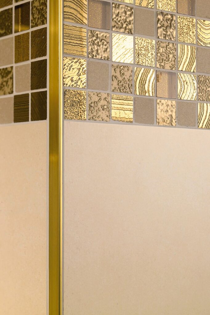 Close up praktijkfoto van L-profiel tegelprofiel messing, hoek van muur. Op de foto zijn ook kleine tegels te zien in messing ofwel gouden uitvoering.